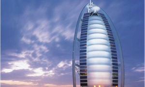 a tall building with a curved roof with Burj Al Arab in the background