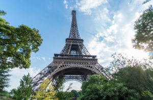 a tall metal tower with trees and blue sky with Eiffel Tower in the background