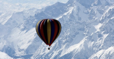 a hot air balloon in the air over snowy mountains