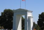 a white arch with flags on top with Peace Arch in the background