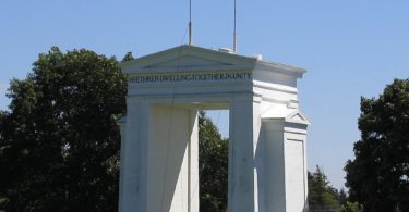 a white arch with flags on top with Peace Arch in the background