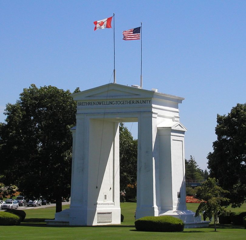 a white arch with flags on top with Peace Arch in the background