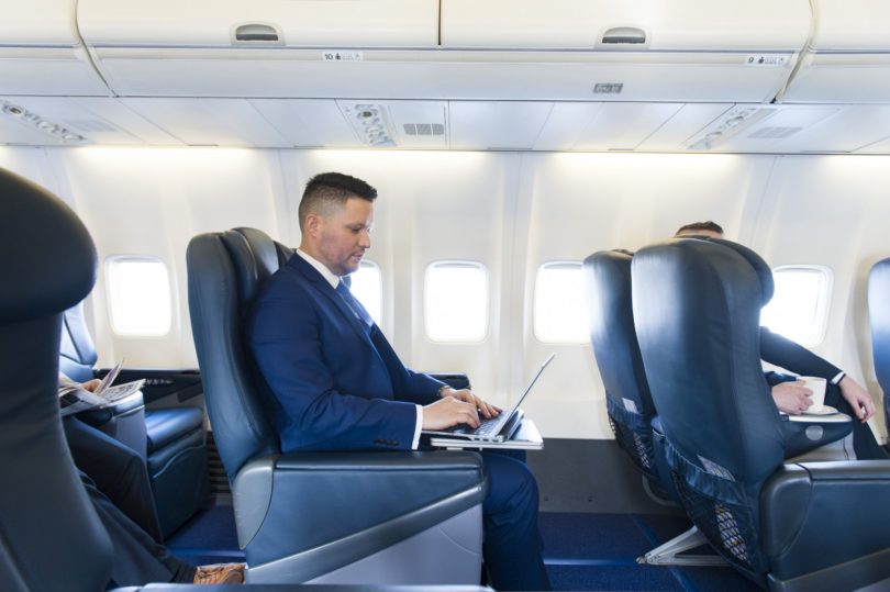 a man in a suit using a laptop on an airplane