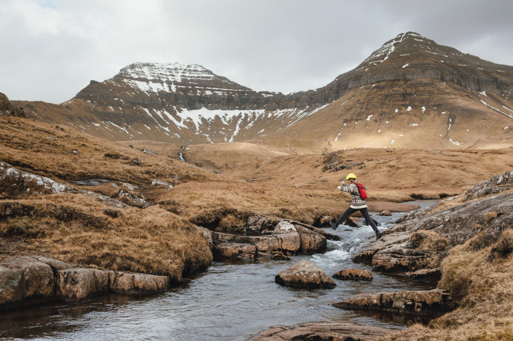 a person crossing a river in a valley with mountains in the background