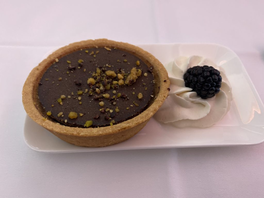 a small chocolate tart with whipped cream and a blackberry on a white plate