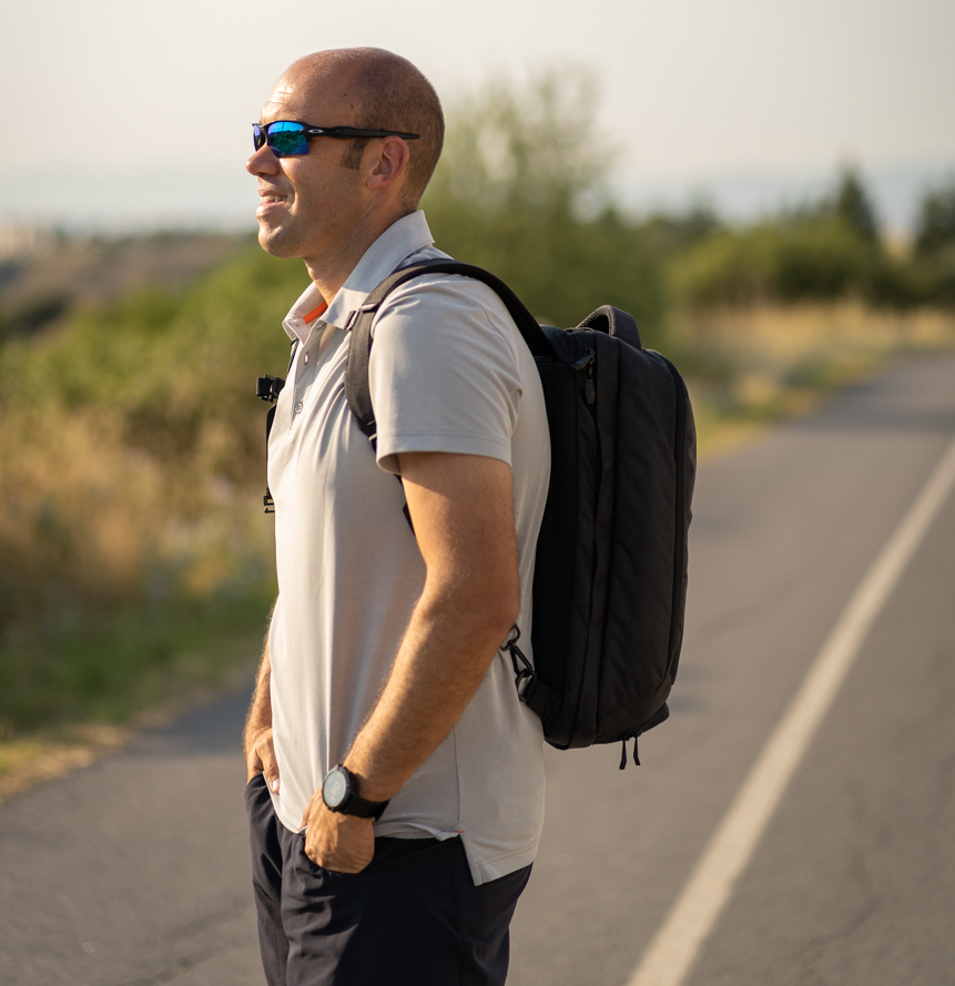 a man wearing sunglasses and a backpack walking on a road