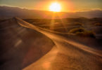 a sand dunes with the sun setting behind them