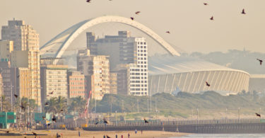 a beach with a large white arch and buildings in the background
