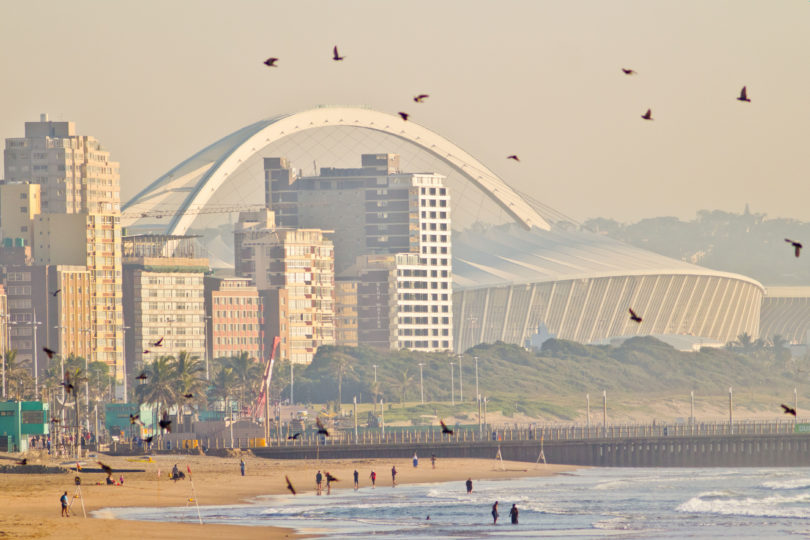 a beach with a large white arch and buildings in the background