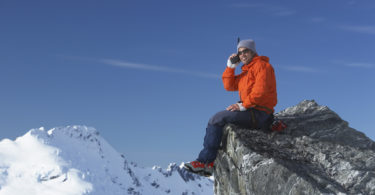 a man sitting on a rock with snow covered mountains in the background