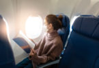 a woman wearing a mask reading a book on an airplane