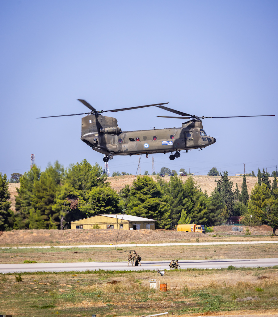 a military helicopter flying over a runway