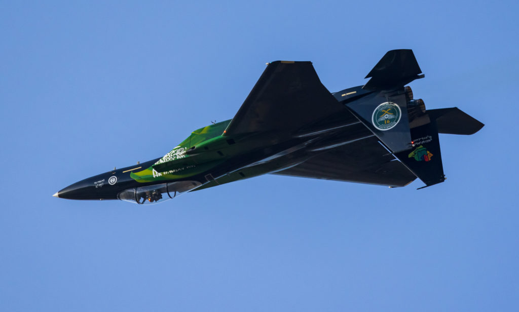 a green and black jet flying in the sky