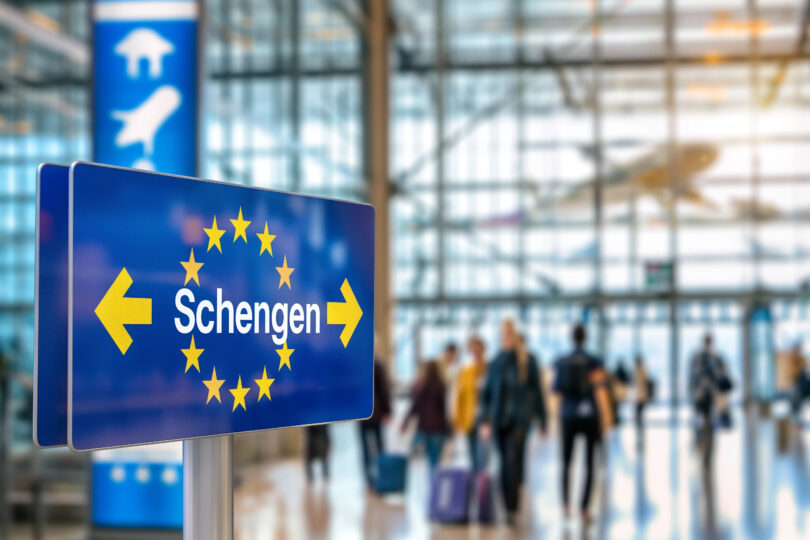 a blue sign with yellow stars and arrows in a building with people in the background