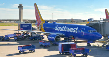 a blue airplane with luggage carts and a tower