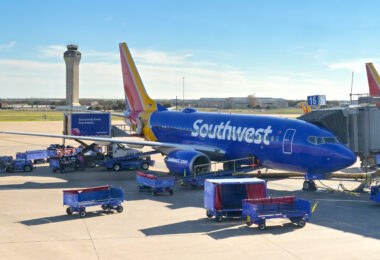 a blue airplane with luggage carts and a tower