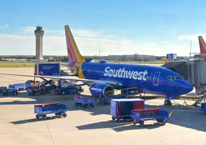 a blue airplane with luggage carts and a tower