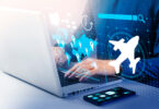A person is using a laptop with digital graphics overlaid, including a world map with location pins, a clock, a search bar, and an airplane icon. A smartphone with app icons is on the table next to the laptop. The image suggests themes of travel, technology, and global connectivity.