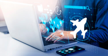 A person is using a laptop with digital graphics overlaid, including a world map with location pins, a clock, a search bar, and an airplane icon. A smartphone with app icons is on the table next to the laptop. The image suggests themes of travel, technology, and global connectivity.