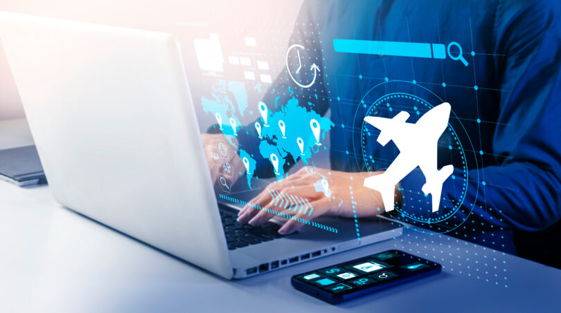 A person is using a laptop with digital graphics overlaid, including a world map with location pins, a clock, a search bar, and an airplane icon. A smartphone with app icons is on the table next to the laptop. The image suggests themes of travel, technology, and global connectivity.