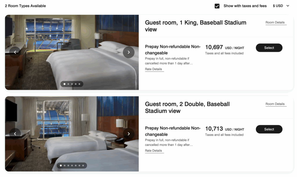 The image shows a hotel booking page with two room options available. The first option is a guest room with one king bed and a view of a baseball stadium, priced at 10,697 USD per night. The second option is a guest room with two double beds and a baseball stadium view, priced at 10,713 USD per night. Both options are non-refundable and non-changeable. Each room has a photo showing a modern interior with a large window overlooking the stadium. There are buttons for selecting each room and viewing more details.
