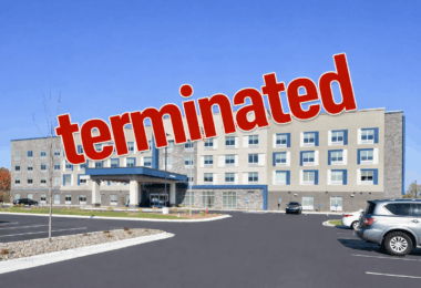 A modern, multi-story hotel building with a large parking lot in front. The sky is clear and blue. Superimposed over the image is the word "terminated" in large, bold red letters.